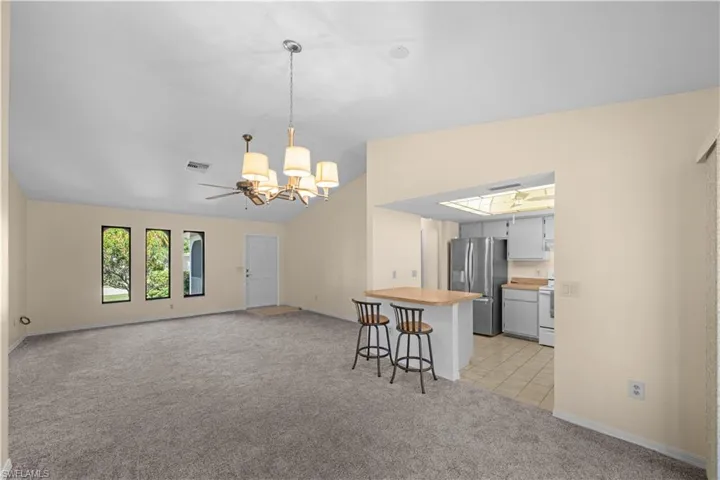 Kitchen with light carpet, lofted ceiling, open floor plan, pendant lighting, and stainless steel fridge with ice dispenser