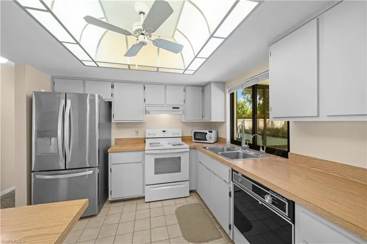 Kitchen with white appliances, light countertops, light tile patterned floors, ceiling fan, and white cabinetry