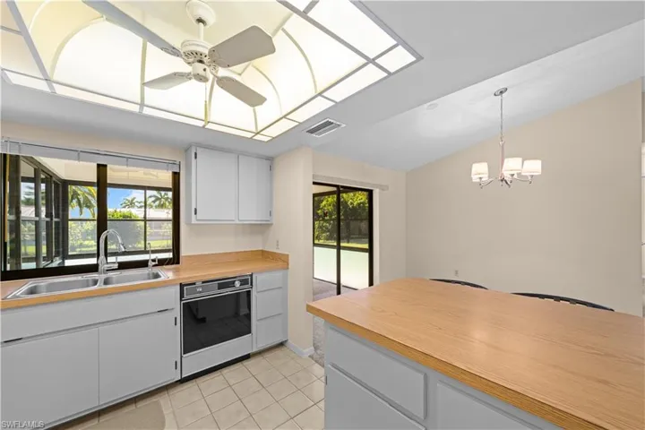 Kitchen featuring white cabinetry, vaulted ceiling, light tile patterned floors, pendant lighting, and oven