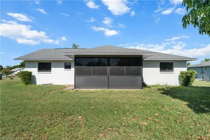 Back of property with a sunroom, stucco siding, a lawn, and a shingled roof