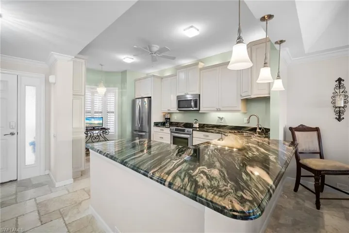 Kitchen featuring crown molding, a peninsula, stone tile flooring, decorative light fixtures, and stainless steel appliances