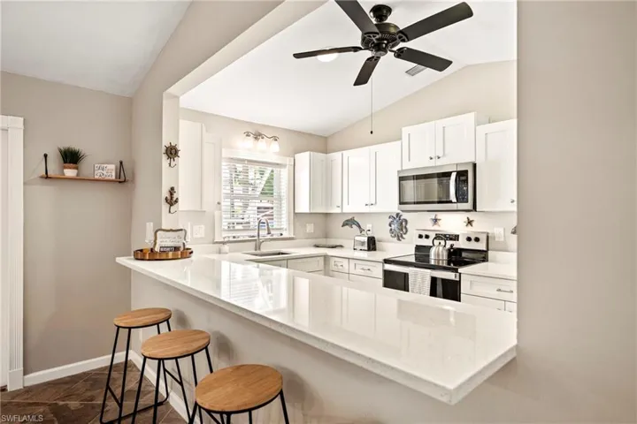Kitchen featuring stainless steel appliances, white cabinetry, a kitchen breakfast bar, a ceiling fan, and light stone countertops