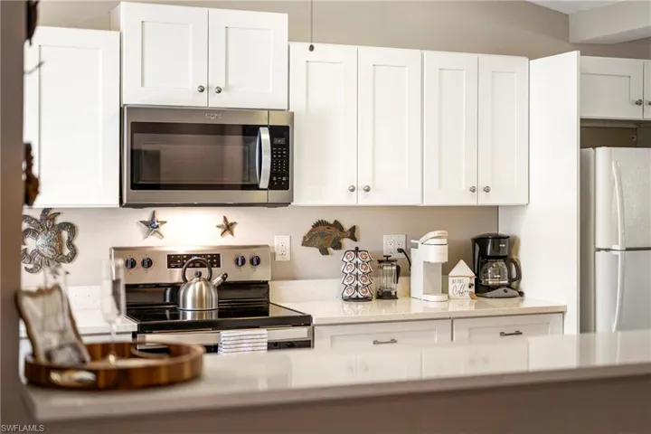 Kitchen featuring stainless steel appliances, white cabinets, and light stone counters