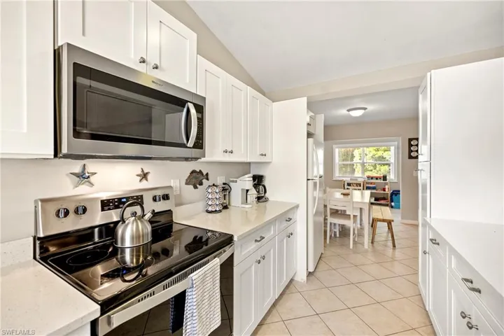 Kitchen featuring stainless steel appliances, white cabinetry, light stone countertops, and lofted ceiling