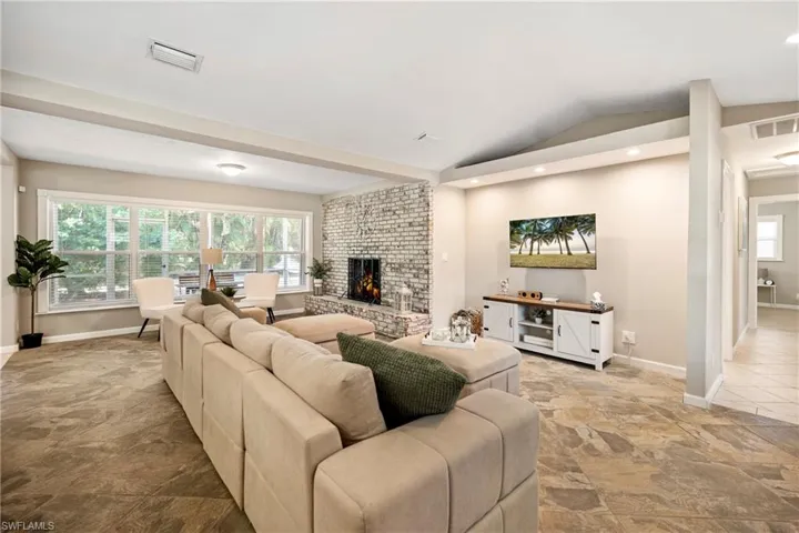 Living area featuring a brick fireplace, lofted ceiling, stone finish floors, and recessed lighting