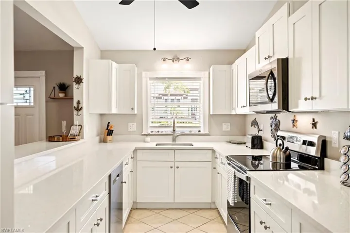 Kitchen featuring stainless steel appliances, white cabinets, light stone countertops, and light tile patterned floors