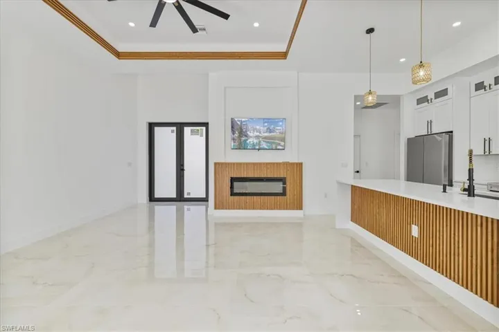 Kitchen with glass insert cabinets, white cabinetry, open floor plan, light marble finish flooring, and decorative light fixtures