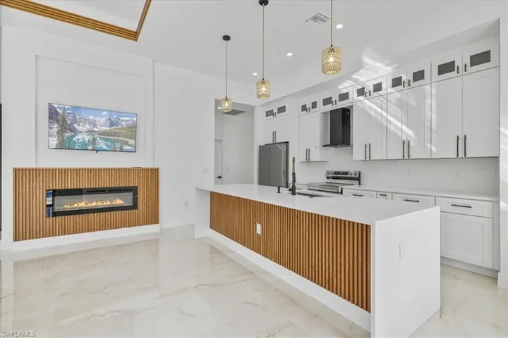 Kitchen featuring white cabinetry, decorative light fixtures, appliances with stainless steel finishes, wall chimney exhaust hood, and light stone countertops