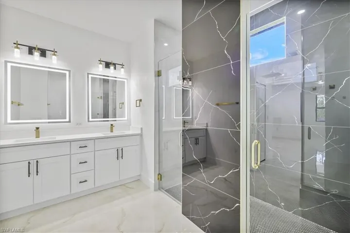 Bathroom featuring double vanity, a marble finish shower, and light marble finish flooring