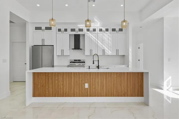 Kitchen with light stone counters, white cabinetry, appliances with stainless steel finishes, a large island, and recessed lighting