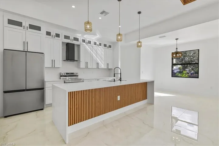 Kitchen featuring stainless steel appliances, white cabinetry, light marble finish flooring, wall chimney range hood, and pendant lighting