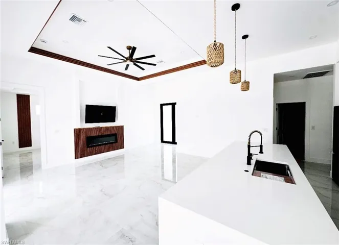 Kitchen with white cabinets, hanging light fixtures, appliances with stainless steel finishes, wall chimney exhaust hood, and light stone counters