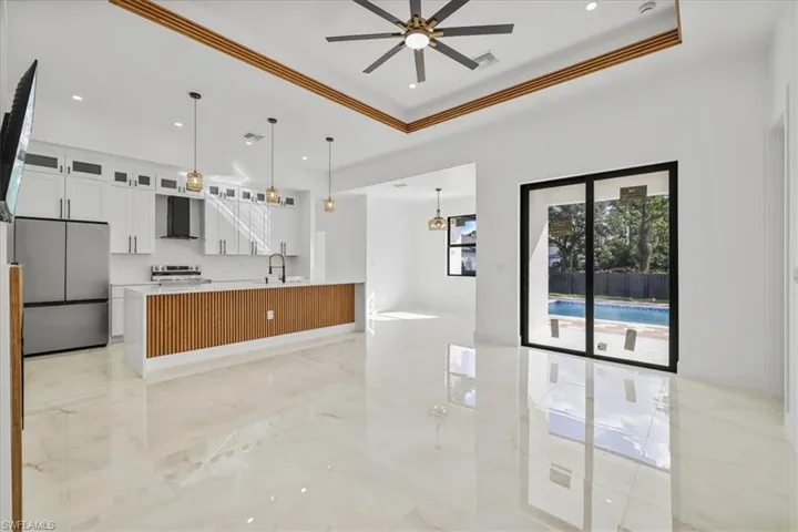 Kitchen featuring glass insert cabinets, white cabinets, appliances with stainless steel finishes, open floor plan, and wall chimney range hood