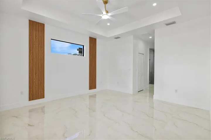 Empty room with a raised ceiling, recessed lighting, light marble finish flooring, and a ceiling fan