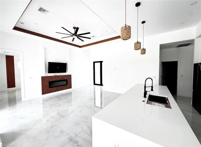 Kitchen with glass insert cabinets, white cabinetry, open floor plan, light marble finish flooring, and decorative light fixtures