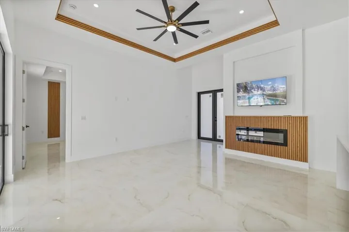 Unfurnished living room featuring light marble finish flooring, french doors, recessed lighting, a glass covered fireplace, and a tray ceiling