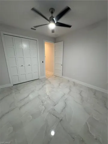 Unfurnished bedroom with light marble finish flooring, a closet, and a ceiling fan