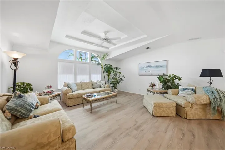 Bright living space featuring wood-finish flooring, a tray ceiling with a fan, and an arched window with white blinds
