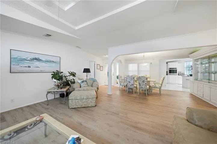 Open-concept living area featuring wood-finish flooring, a tray ceiling, and a large arched entryway leading to the dining space
