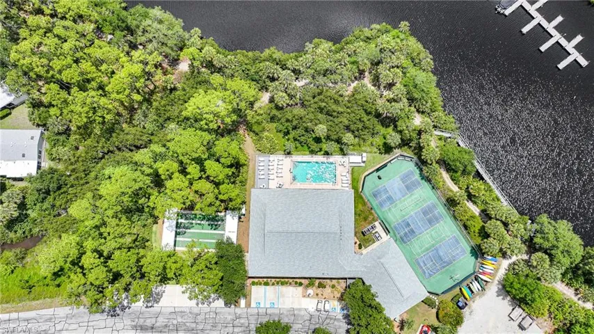 Expansive recreational area featuring a swimming pool with surrounding lounge chairs, multiple tennis courts, a sports court, and direct water access with boat slips and stored kayaks