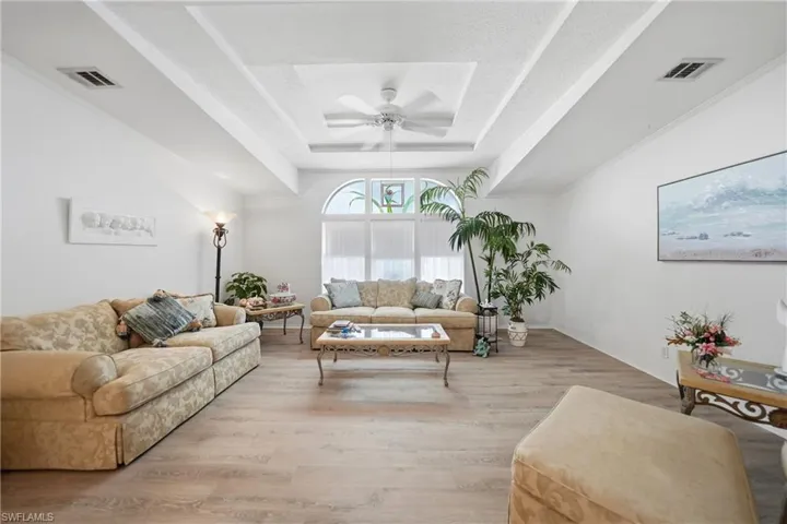 Expansive living area featuring a tray ceiling with a built-in ceiling fan, light wood-finish flooring, and white walls
