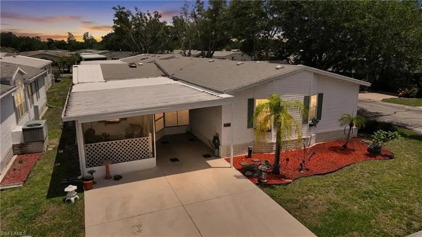 White-sided residence with an attached carport, screened-in patio, and a manicured front yard featuring tropical plantings and red mulch