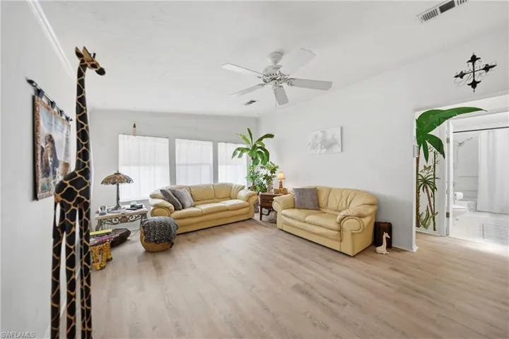 Spacious room featuring light wood-finish flooring, white walls, and a white ceiling fan