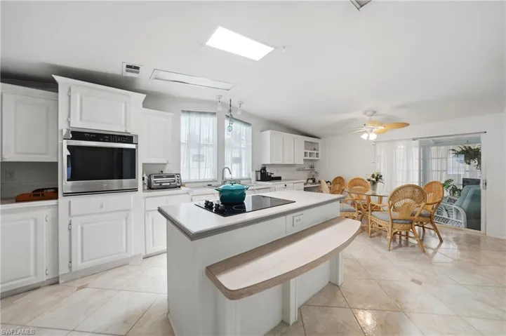 Bright kitchen featuring an island with a built-in cooktop, white cabinetry, integrated stainless steel oven, skylight, and tile flooring