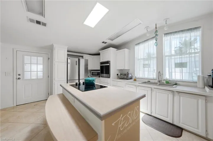 Bright kitchen featuring white cabinetry, a central island with an integrated cooktop, stainless steel appliances, and dual windows above the sink