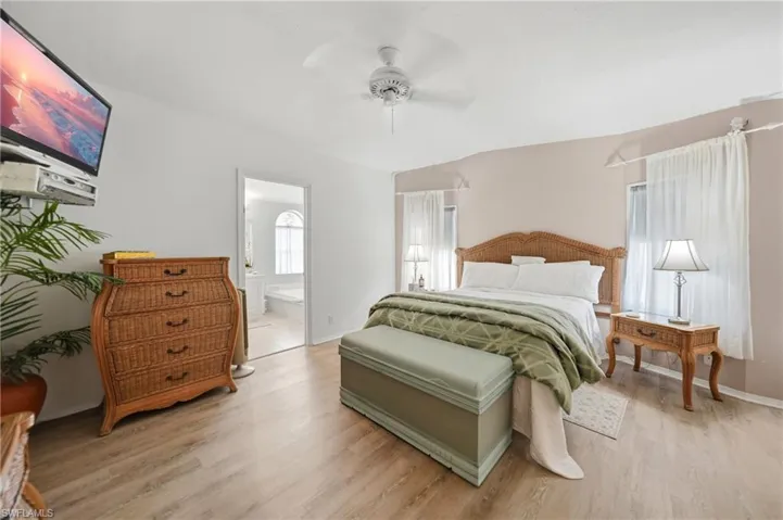 Spacious bedroom featuring wood-finish flooring, a ceiling fan, and multiple windows with sheer curtains