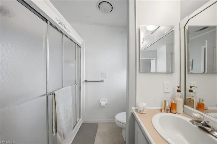 Bathroom featuring a shower with sliding frosted glass doors, a single vanity with an integrated sink, and an overhead lighting fixture