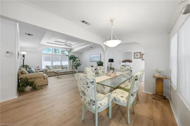 Open-concept living and dining areas featuring wood-finish flooring, arched doorways, a tray ceiling with a ceiling fan, and large arched windows