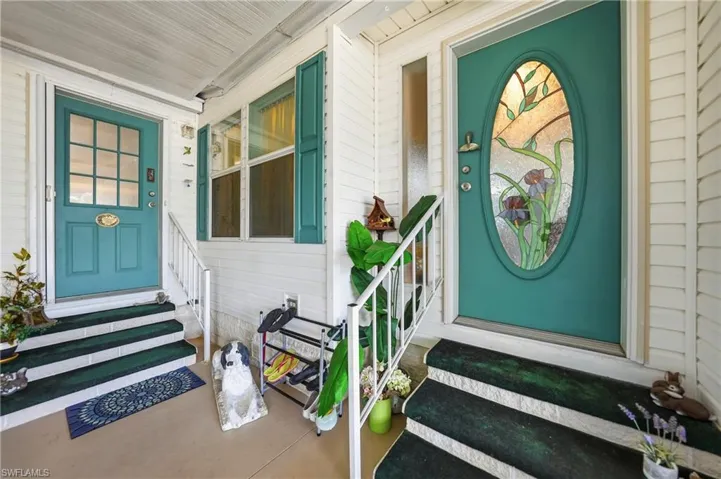 Entryway featuring a teal door with decorative stained glass, white siding, and green shutter accents