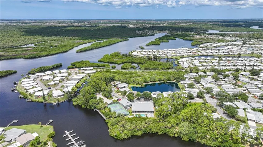 Aerial perspective showcasing a waterfront community with extensive water access, dense green foliage, numerous single-story properties, an aquatic feature, and an on-site tennis court