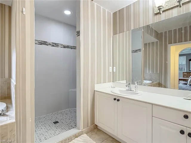 Bathroom with tiled shower, vanity, and tile patterned floors