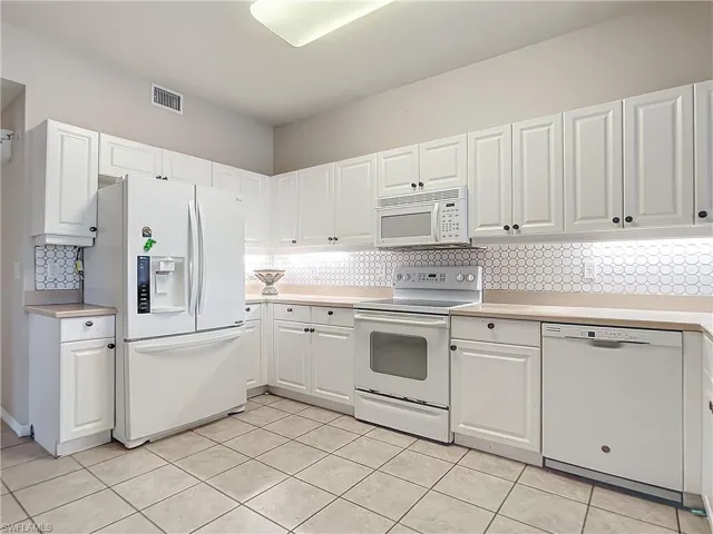 Kitchen featuring backsplash, white cabinetry, light tile patterned floors, and white appliances