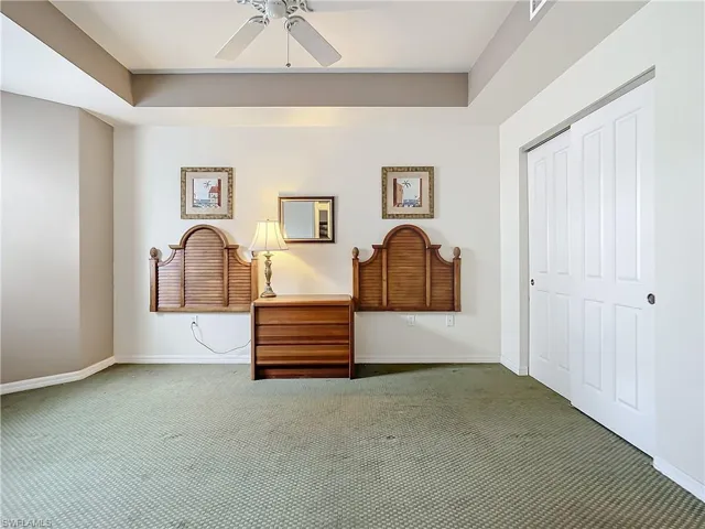 Unfurnished Guest bedroom with a closet, dark carpet, ceiling fan, and a tray ceiling