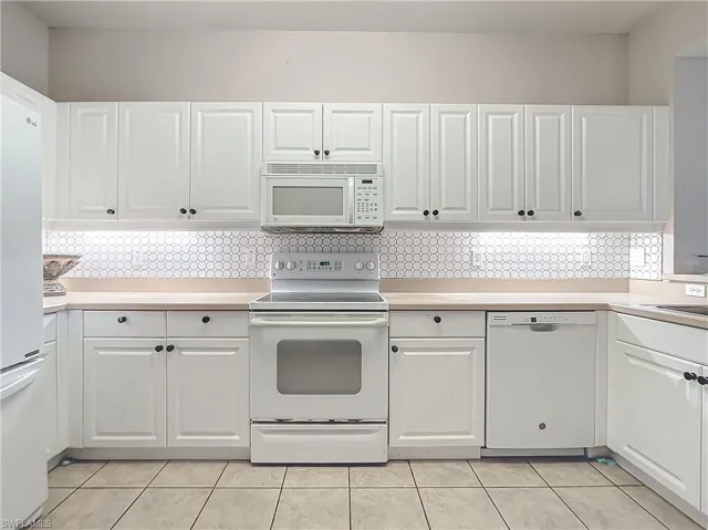 Kitchen with backsplash, white cabinetry, and white appliances