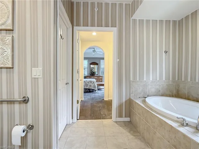 Bathroom with tile patterned flooring, ceiling fan, and tiled bath