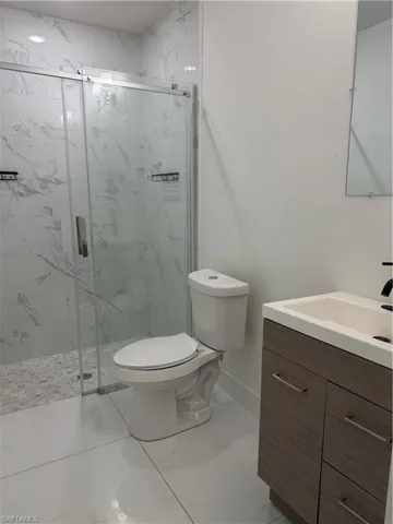 Glass-enclosed shower with large format tile surround, pebble tile shower floor, and recessed lighting