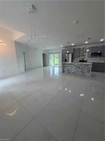 Spacious open-concept interior featuring large format tile flooring, a kitchen island with stone veneer, and stainless steel appliances