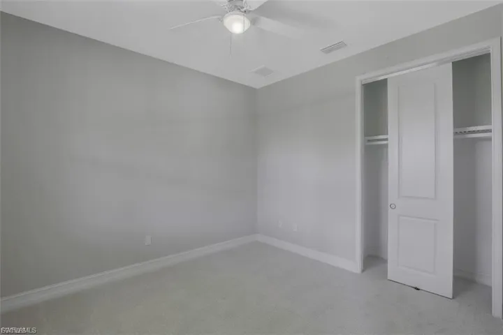Unfurnished bedroom featuring light colored carpet, a closet, and ceiling fan
