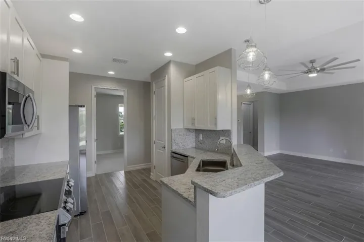 Kitchen with light stone counters, wood finish floors, pendant lighting, backsplash, and ceiling fan