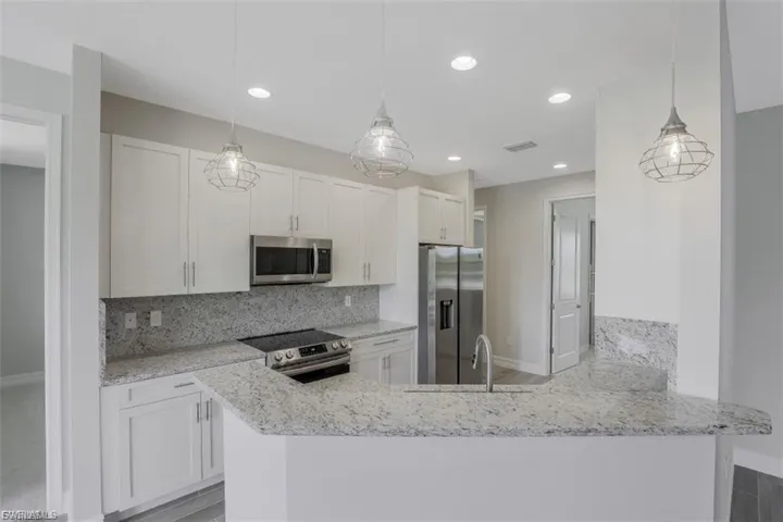 Kitchen featuring stainless steel appliances, pendant lighting, light stone counters, white cabinetry, and a peninsula