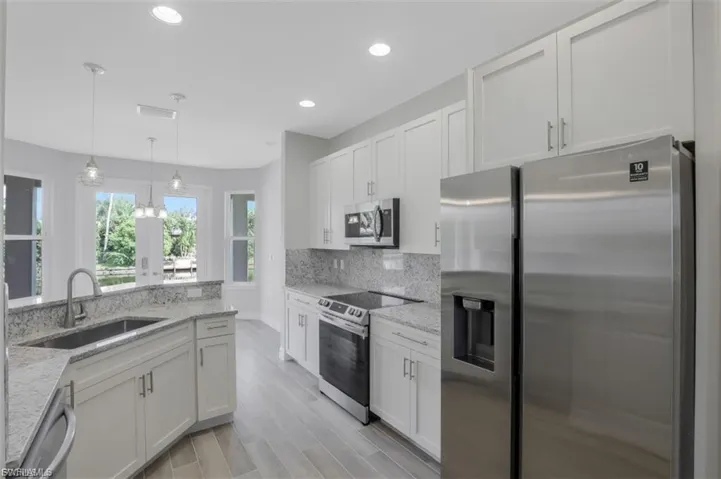 Kitchen with stainless steel appliances, white cabinetry, light stone countertops, decorative light fixtures, and light wood-type flooring
