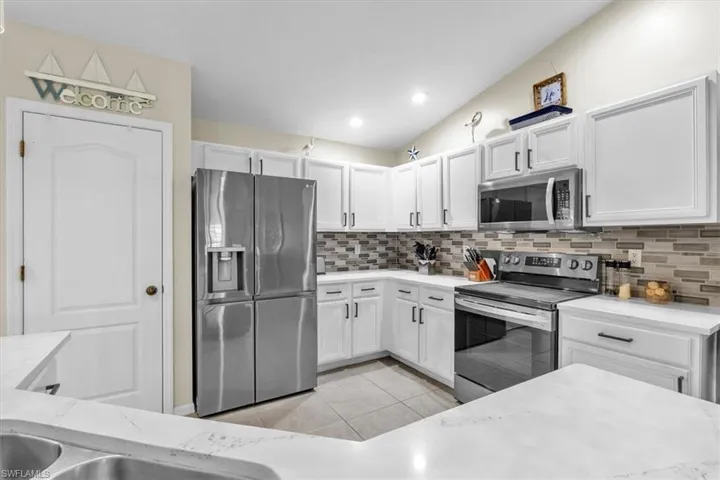 Kitchen featuring white cabinetry, stainless steel appliances, mosaic tile backsplash, white countertops, and recessed lighting