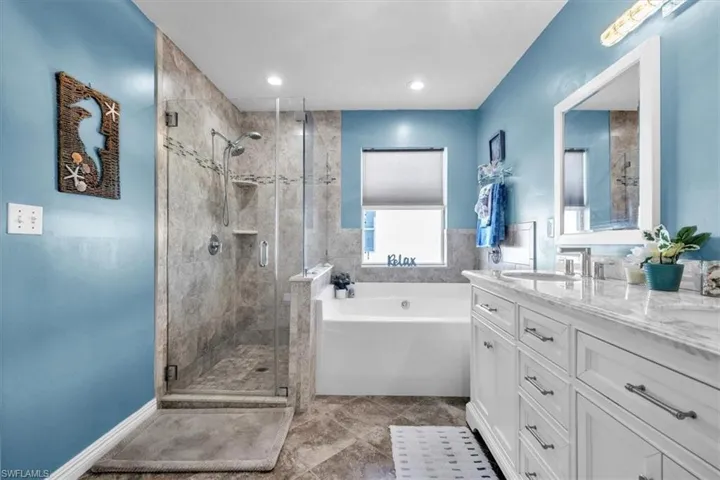 Glass-enclosed walk-in shower with tile surround, soaking tub, dual-sink vanity with stone countertop, and wood-finish flooring