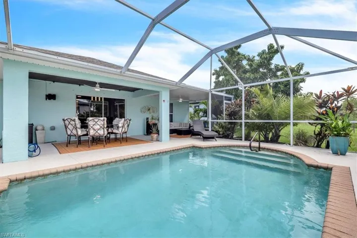 Screened-in outdoor living space featuring a swimming pool with integrated steps, brick coping, and a covered patio area with a ceiling fan