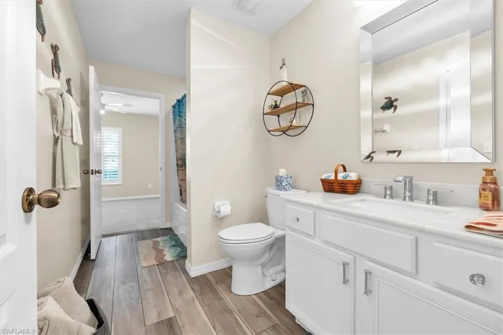 Wood-finish flooring, white vanity with integrated sink, rectangular framed mirror, and a built-in bathtub
