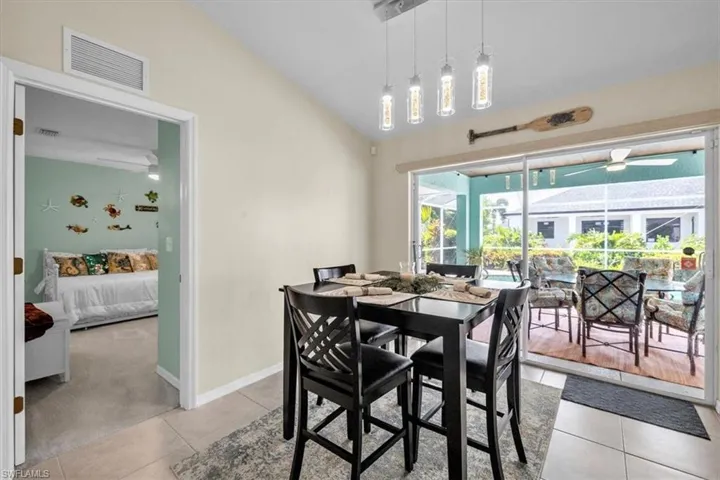 Vaulted ceiling with an attached linear pendant light fixture, featuring large format tile flooring, and a sliding glass door to an outdoor screened area